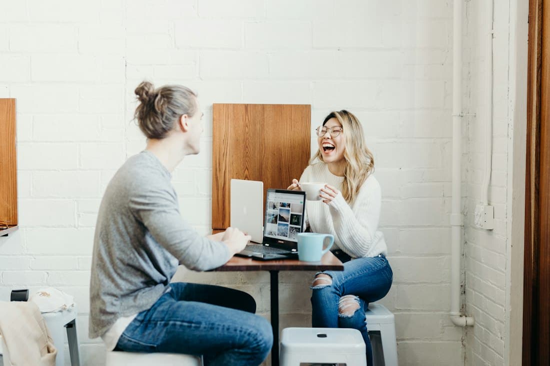 Two young people laughing over coffee at a cafe table